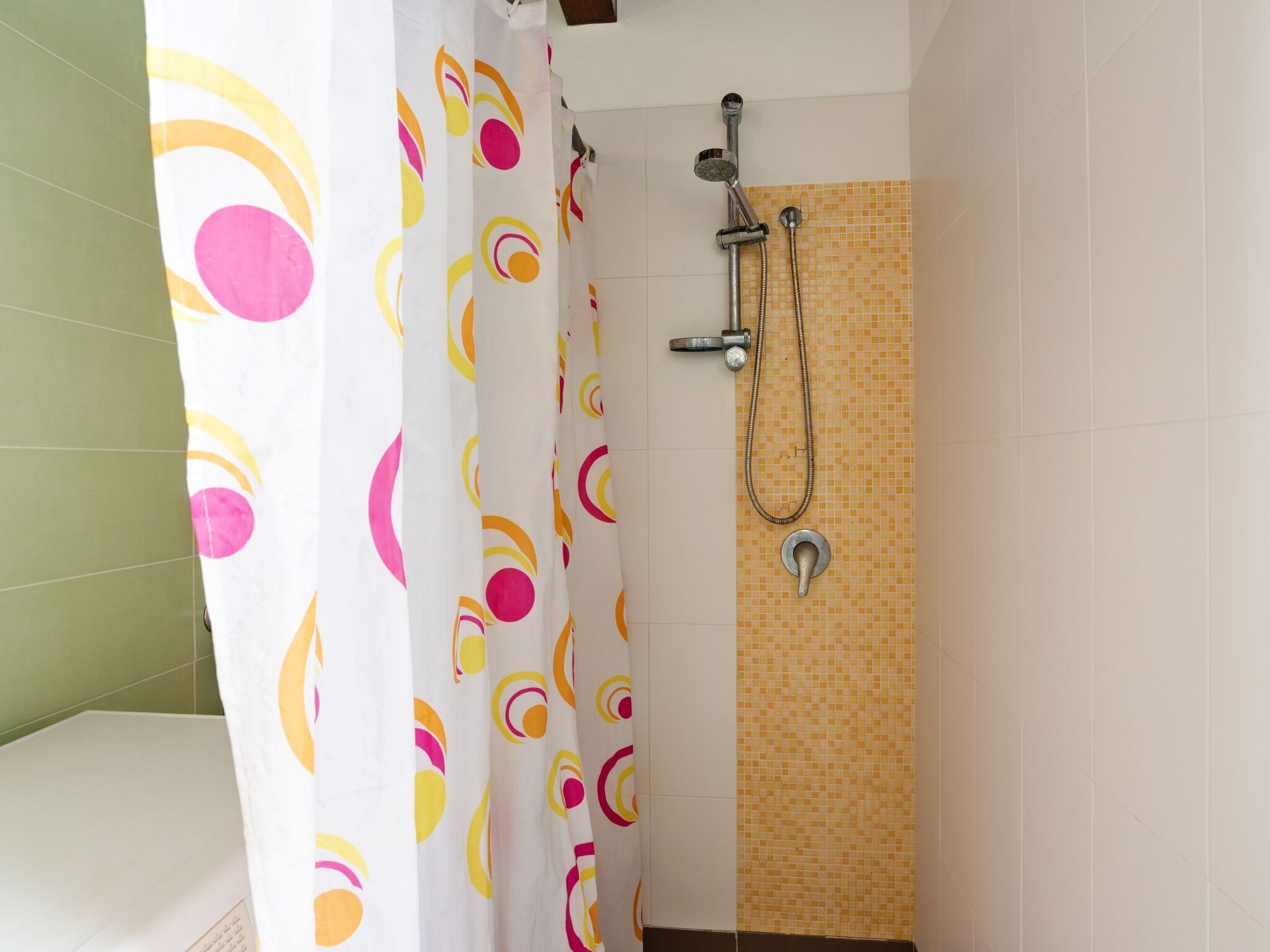 A bathroom with a shower, a curtain with colorful patterns, and tiled walls.