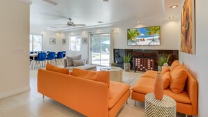 A modern living room with orange sofas, a fireplace, and a dining area with blue chairs.