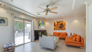 A spacious living room with a ceiling fan, a grey sofa, an orange sofa, and a fireplace.
