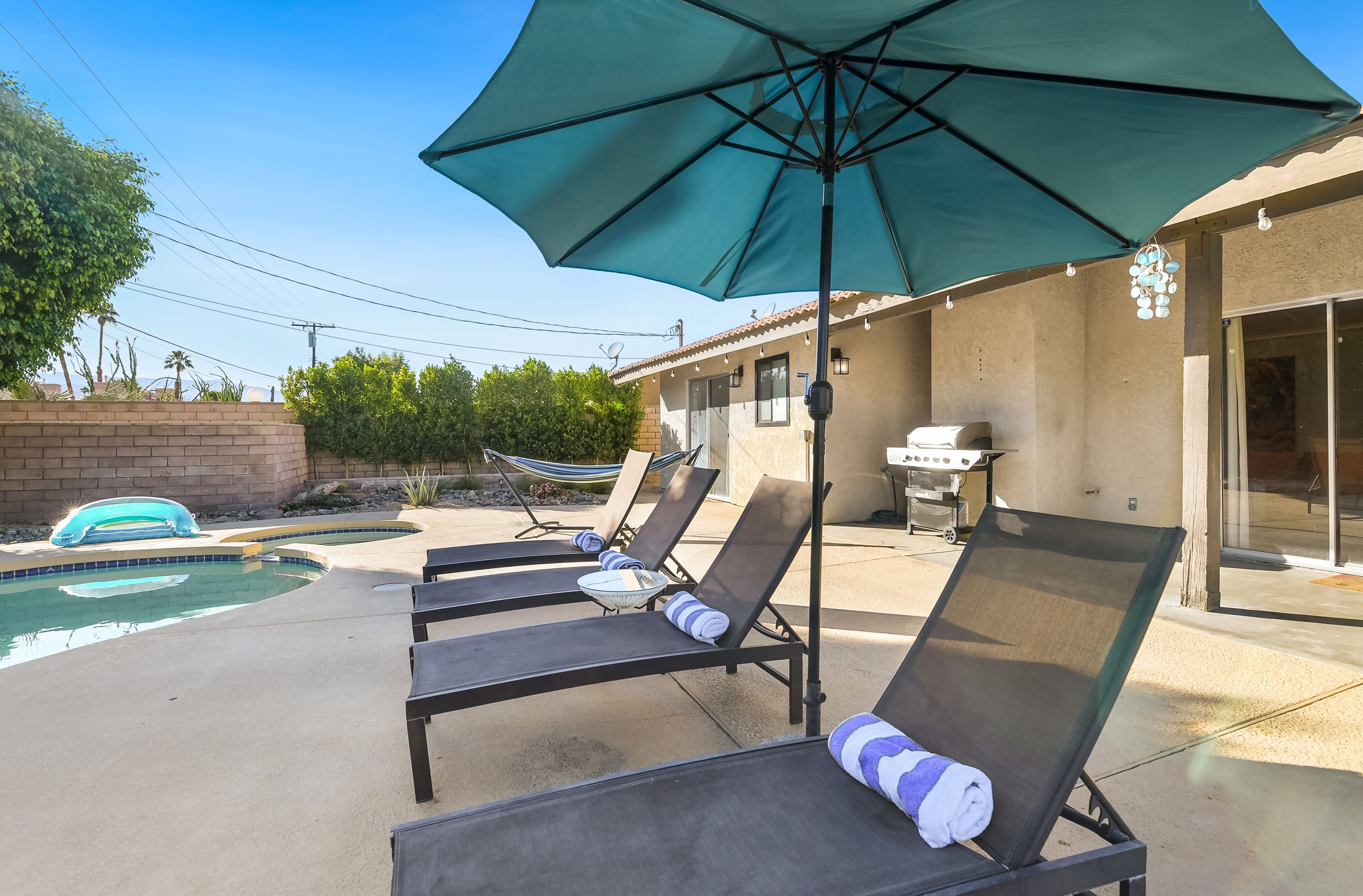 A poolside area with lounge chairs, a large umbrella, and a barbecue grill.