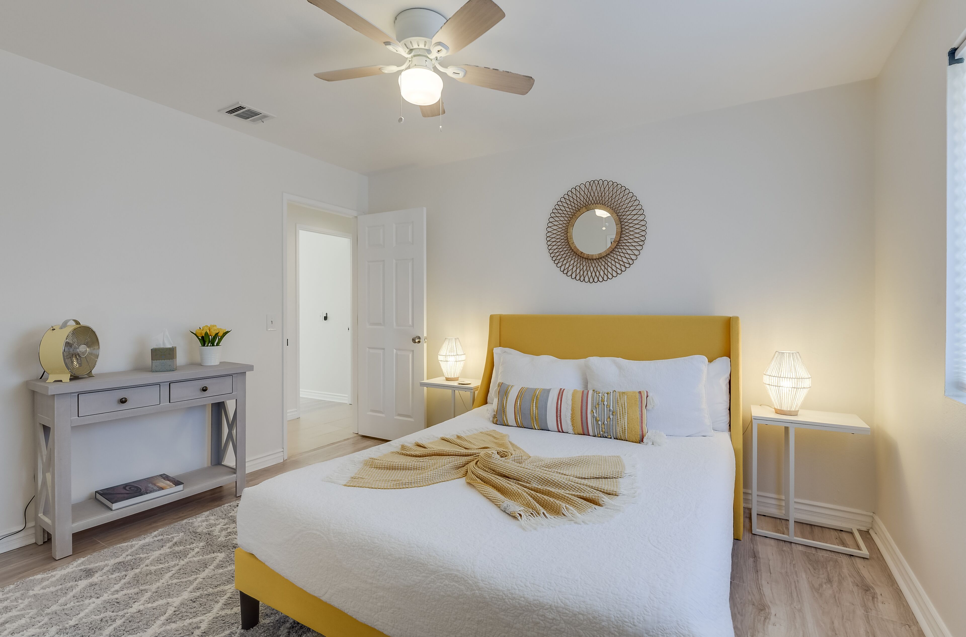 A bedroom with a bed, bedside lamps, a ceiling fan, a bedside table, and a wall decoration.