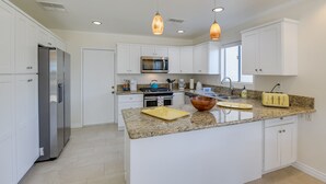 A modern kitchen with white cabinets, granite countertops, stainless steel appliances, and pendant lighting.