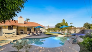 A backyard with a swimming pool, lounge chairs, and a hammock.