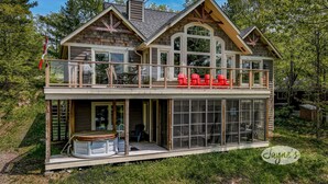 Eine zweistöckige Holzhütte mit einem Balkon, großen Fenstern und einer Terrassenfläche.