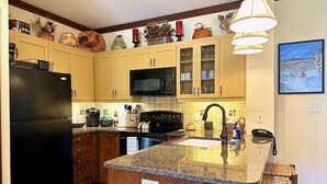 Una cocina con armarios de madera, un refrigerador negro, un microondas y una encimera de granito.