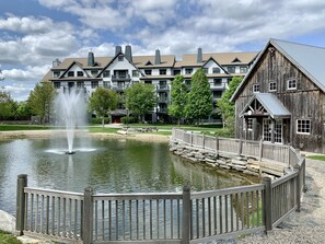 Vista del lago con un edificio de madera, una fuente y un hotel de varios pisos al fondo.