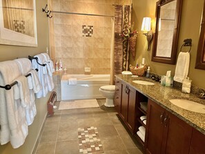 Un baño con bañera, inodoro y lavabo, que presenta un suelo de baldosas estampadas y toallas en un tendedero.