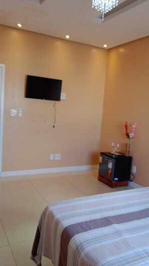 A hotel room with a bed, a TV mounted on the wall, a small cabinet, and a vase with flowers.