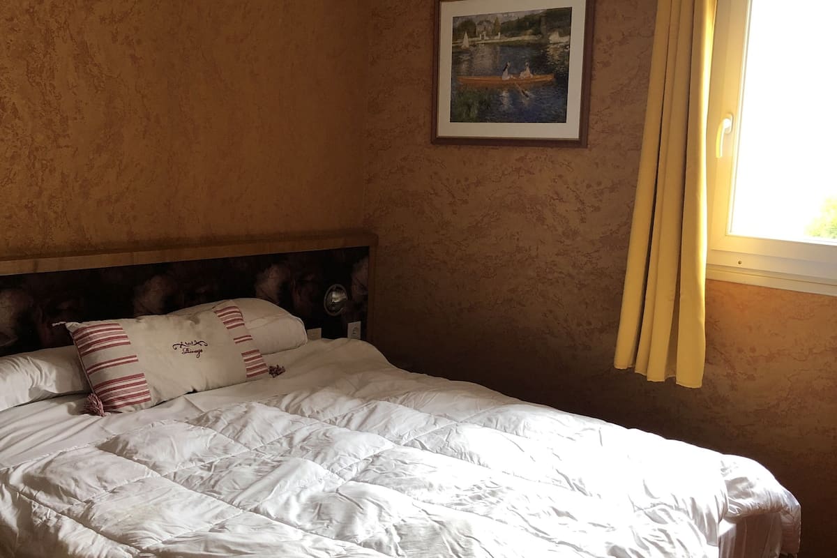 A bedroom with a large bed, a headboard, a framed picture on the wall, and a window with curtains.