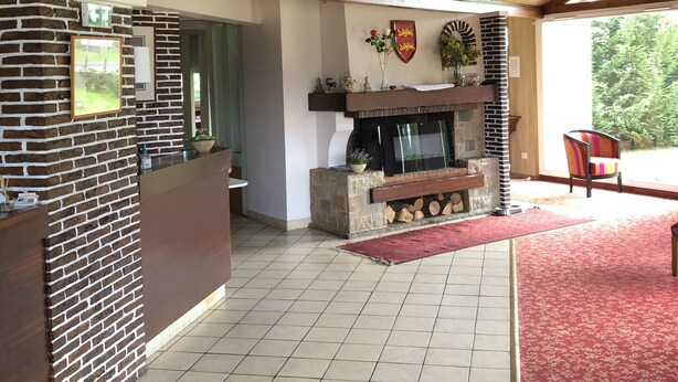 A reception area with a brick wall, a wooden reception desk, a fireplace, and a red carpet. - Hotel Le Drakkar (Pont-Audemer)