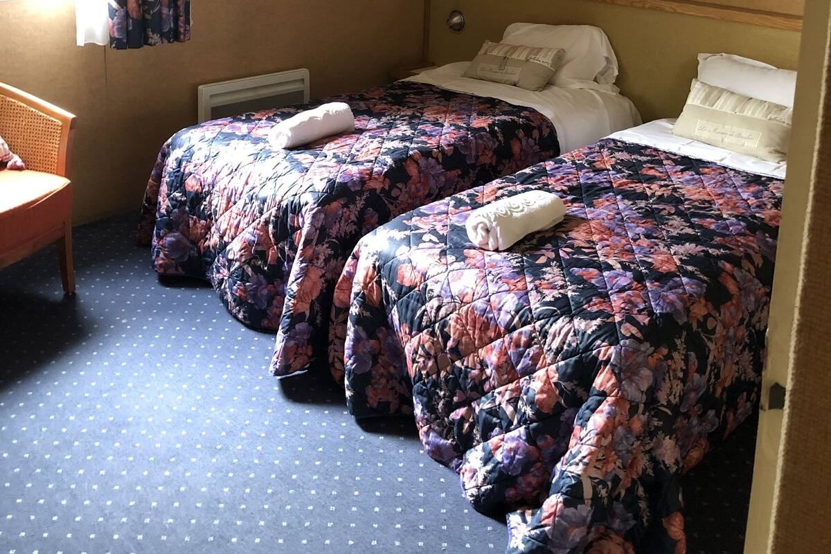 A hotel room with two beds, a chair, a framed picture on the wall, and a window with curtains.