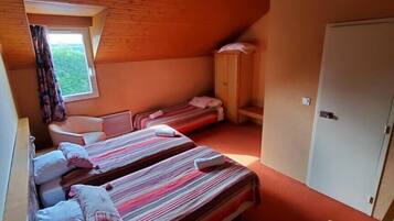 A small, cozy room with two beds, a window, a door, and a chair.
