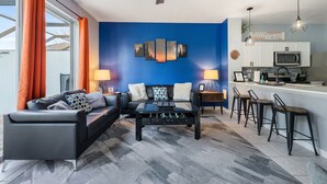 A modern living room with a black sofa, a coffee table, and a blue accent wall. - StarWars Theme + Free Waterpark | 10 min to Disney (Kissimmee)