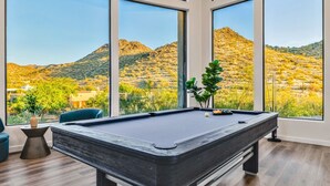 Una mesa de billar en una habitación con ventanas amplias que dan a un paisaje desértico.