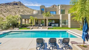 Una casa moderna con piscina, mobiliario de exterior y montañas al fondo.