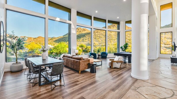 Un amplio salón con una gran mesa de comedor, asientos cómodos y vistas a un paisaje montañoso a través de amplias ventanas.