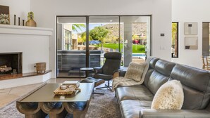 Una sala de estar moderna con chimenea, sofá de cuero y vistas a una piscina y jardín.