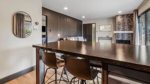 Una cocina moderna con encimera oscura, taburetes de bar y horno empotrado.