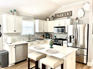 A modern kitchen with white cabinetry, a stainless steel refrigerator, a microwave, and a stove.