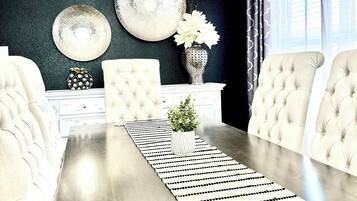 Un salon moderne avec un mur d’accent de couleur foncée, un lustre et un coin repas agrémenté d’un tapis à rayures.