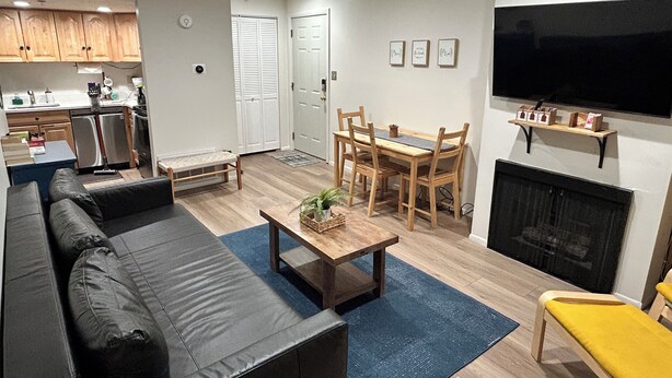A modern living room with a sofa, a coffee table, and a fireplace. There is a dining area with a table and chairs. The room has wooden flooring and white walls. - Cozy Freshly remodeled 1B/1B Retreat close to Main (Park City)