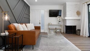 A modern living room with a sofa, a glass coffee table, a fireplace, and a mounted TV.