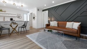 A modern living room with a brown leather sofa, a glass coffee table, and a dining area with a round table and chairs.