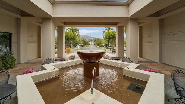 A courtyard with a central fountain, seating areas, and a view of a distant landscape.