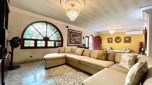 A living room with a large arched window, a chandelier, a sectional sofa, and a small table. - 8MG-1 MANSION EN CARTAGENA CERCA AL MAR (Cartagena)