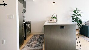 A modern kitchen with a central island, stainless steel appliances, and a hanging light fixture. - New Condo Walkable to Downtown Bozeman (Bozeman)