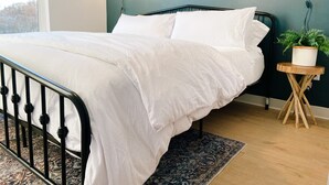 A neatly made bed with white bedding, a dark headboard, and a small wooden side table with a plant. - New Condo Walkable to Downtown Bozeman (Bozeman)