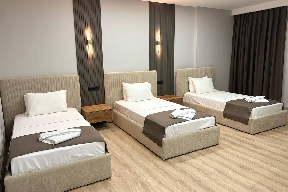 Une chambre d’hôtel avec trois lits disposés en forme de U, chacun étant muni d’une table de chevet en bois et d’une lampe fixée au mur.