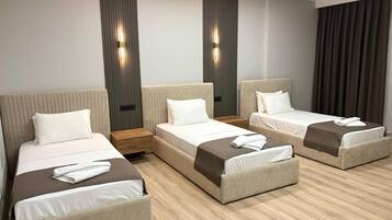 A hotel room with three beds arranged in a U-shape, each with a wooden nightstand and a wall-mounted light.