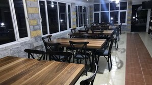 Un restaurant avec de nombreuses tables en bois et des chaises noires, de grandes fenêtres le long d’un mur et un sol carrelé.