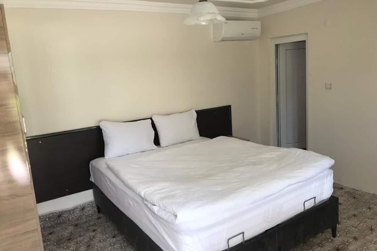 Une chambre à coucher avec un lit, une tête de lit, un luminaire suspendu et une porte.