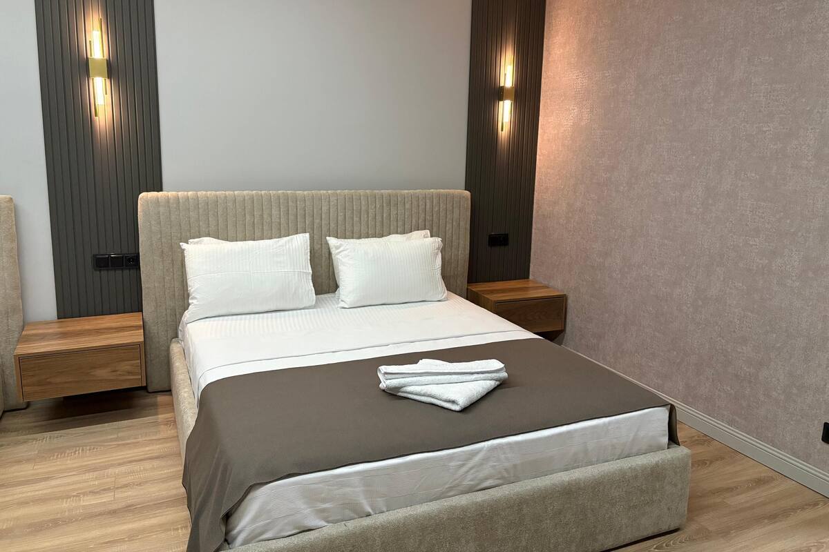 Une chambre moderne avec un grand lit, deux tables de chevet et des lampes fixées au mur.