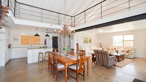 Uma sala ampla com uma mesa de jantar, cadeiras, um sofá e uma mesa de centro. Escada leva a um andar superior.