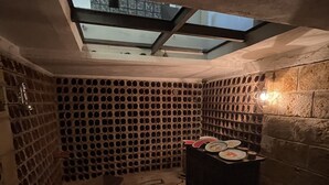 A narrow, dimly lit room with a skylight, a brick wall with circular holes, and a table with plates and a candle. - VILLA ZAGARA (Tipical luxury Sicilian residence) (Sicilia)