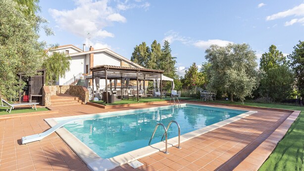 A swimming pool with a patio area, a covered seating area, and a view of trees and a building in the background. - VILLA ZAGARA (Tipical luxury Sicilian residence) (Sicilia)