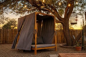 A wooden swing bed with a canopy, surrounded by a wooden fence and a tree.