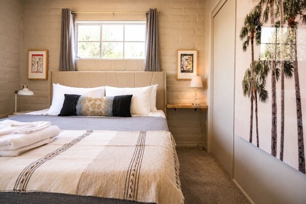 A bedroom with a bed, pillows, a bedside table, a lamp, and a framed picture on the wall.