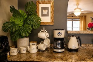 A kitchen counter with a coffee maker, a kettle, and several white mugs with text. - Benton Place - A Stylish Southwest Retreat (Tucson)