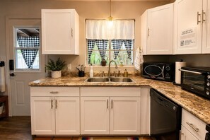 A kitchen with white cabinets, a double sink, a microwave, and a dishwasher.