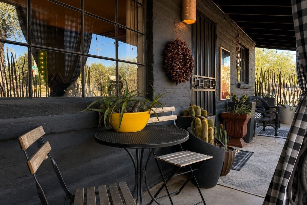 A covered outdoor seating area with a table, chairs, and potted plants.