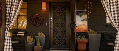 A wooden door with a geometric pattern, flanked by checkered curtains, a wreath, and potted cacti.