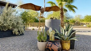 Un jardín de cactus con una escultura de pájaro, una palmera y un edificio al fondo.