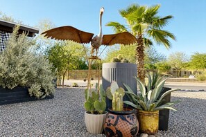 A cactus garden with a bird sculpture, a palm tree, and a building in the background.