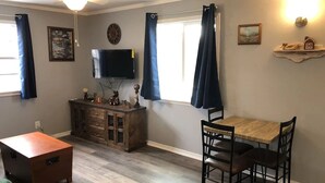 A room with a wooden dining table and chairs, a TV mounted on the wall, a wooden cabinet, and a ceiling fan.