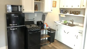 A compact kitchen with a black refrigerator, stove, and microwave. White cabinets and a small trash bin are also visible.