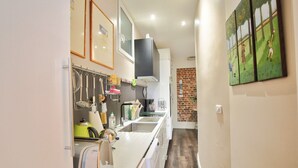 Une cuisine étroite avec un long comptoir, des ustensiles suspendus, une bouilloire et un mur en briques.